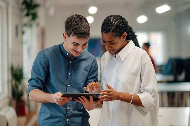 istock Two smiling business colleagues using digital tablet in office hallway 2204354201