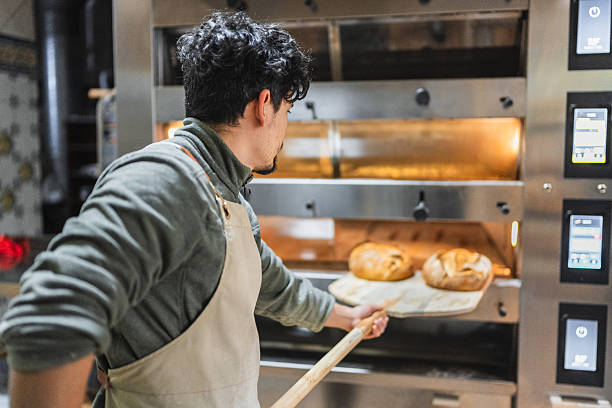 istock Baker taking freshly baked bread out of oven with peel 2204354467