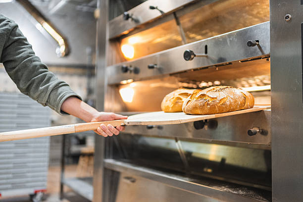 istock Baker taking freshly baked bread out of oven in bakery 2204354512