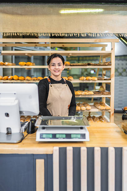 Young female baker smiling behind the counter of a bakery