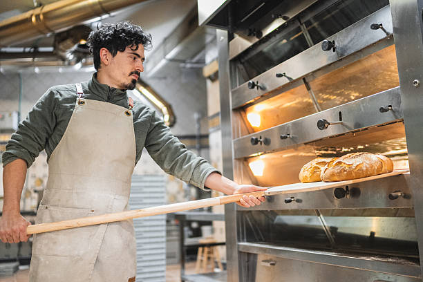 istock Baker taking freshly baked bread out of oven in bakery 2204354519