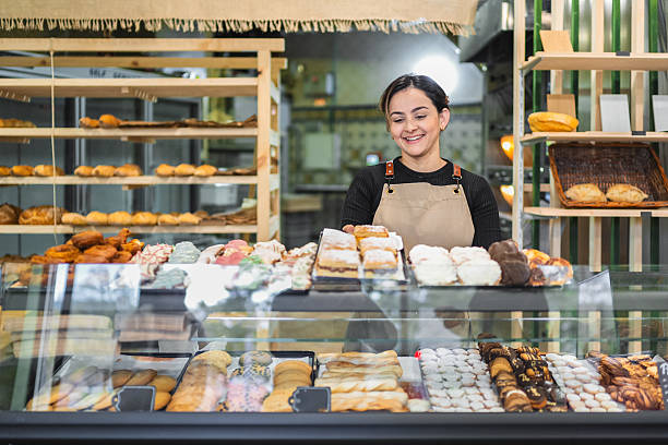 istock Smiling baker arranging pastries in display case at bakery shop 2204354571