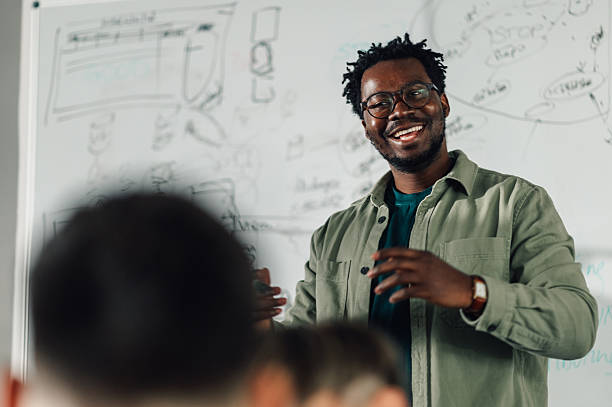 istock Smiling black male teacher explaining lesson to students in classroom 2204358518