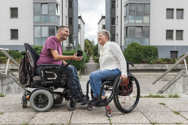 Two friends, wheelchair users on the street, smiling and looking at a smartphone. People with disability and social wellbeing concepts.
