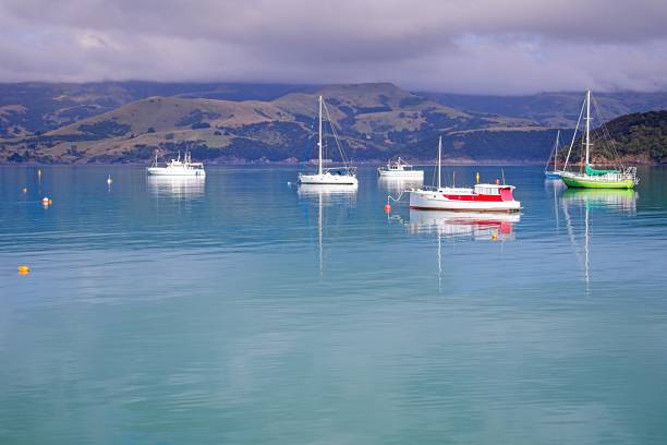 A serene coastal scene featuring several boats anchored in calm turquoise waters, with mountains in the background under a partly cloudy sky.