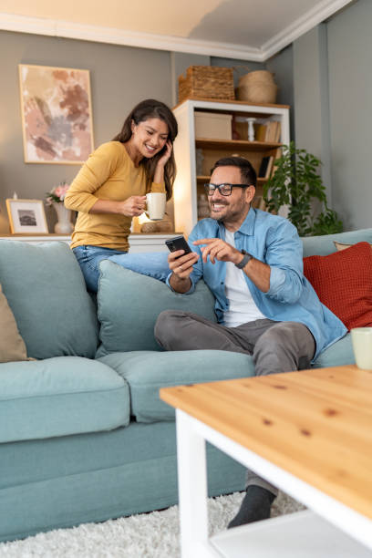 istock Happy couple using phone while relaxing on sofa at home 2204369309