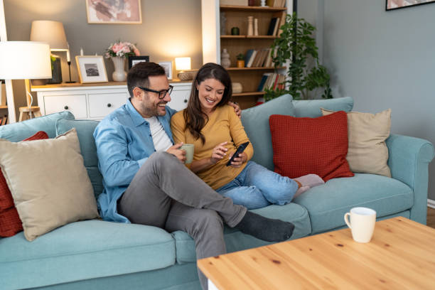 istock Happy couple using phone while relaxing on sofa at home 2204369386