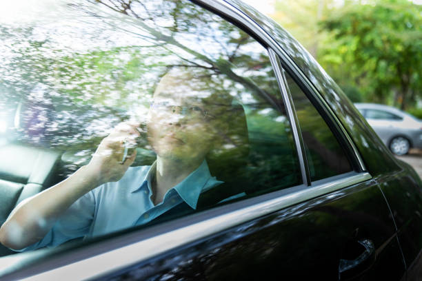 Portrait of a confident, smiling businessman in formal wear driving a car in an urban setting, on a sunny day.