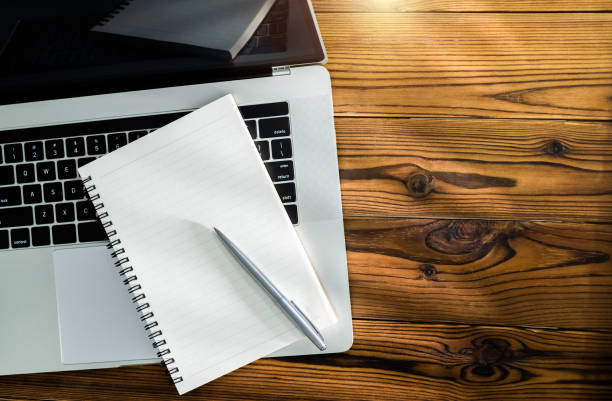 Laptop computer with pen and spiral notebook on desk