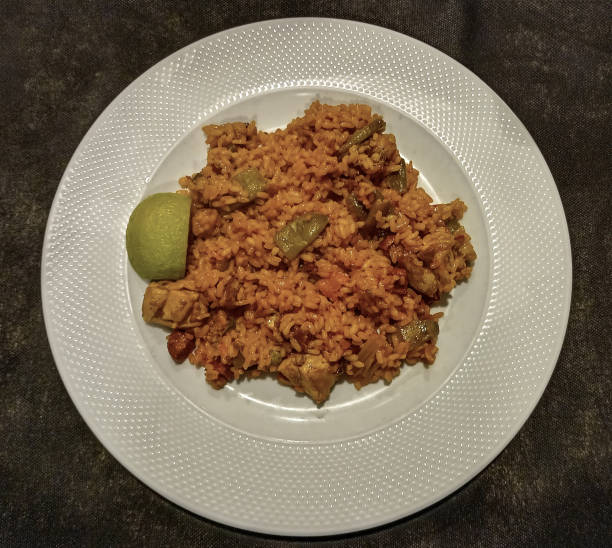 A delicious Spanish rice dish with meat, vegetables, and a lime wedge, served on a white plate.