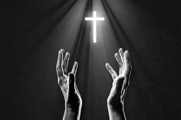 istock Hand Praying to Illuminated Cross in Black and White 2204385246