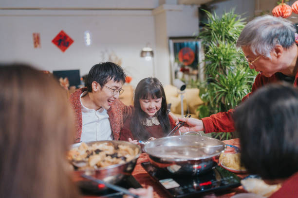 Modern Hong Kong multi-generation family celebrating Chinese New Year. They are enjoying  dinner with hotpot and Big Bowl Feast (poonchoi) , a cantonese cuisine.