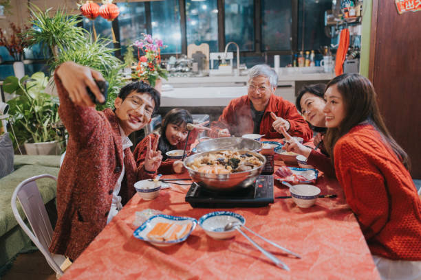 Modern Hong Kong multi-generation family celebrating Chinese New Year. They are having a selfie while  enjoying  dinner with hotpot and Big Bowl Feast (poonchoi) , a cantonese cuisine.