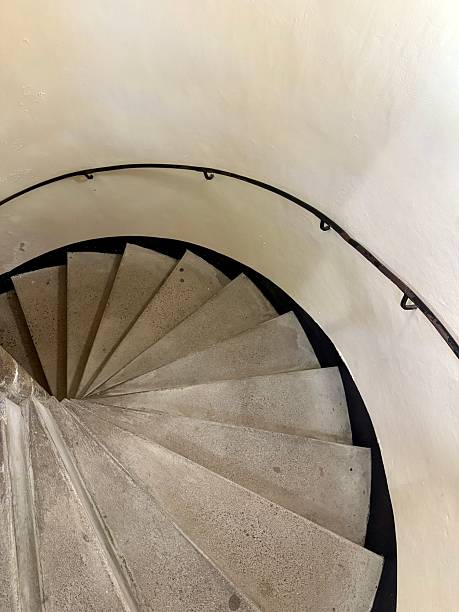 A white spiral stone staircase curves downward with a simple handrail along the white wall.