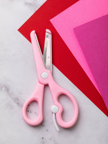 istock Children's pink scissors and colored paper on table, top view 2204393191
