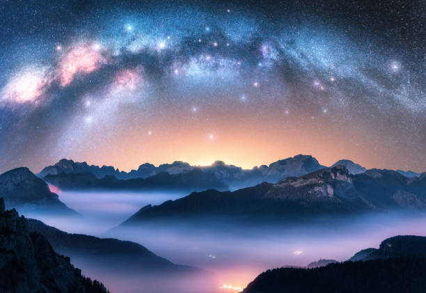 istock Milky Way arch above mountains in low clouds at night. Landscape with alpine mountain valley in fog, starry sky with milky way, illumination. Aerial view. Passo Giau, Dolomites, Italy. Space. Top view 2204393203