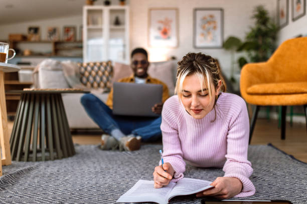istock Portrait of young female student reading book while lying down on floor. 2204393225