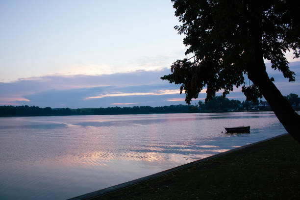 istock Tranquil Lake at Twilight with Silhouetted Tree and Floating Boat 2204393736