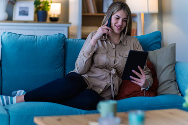 istock Smiling beautiful woman relaxing with digital tablet on couch at home 2204394021