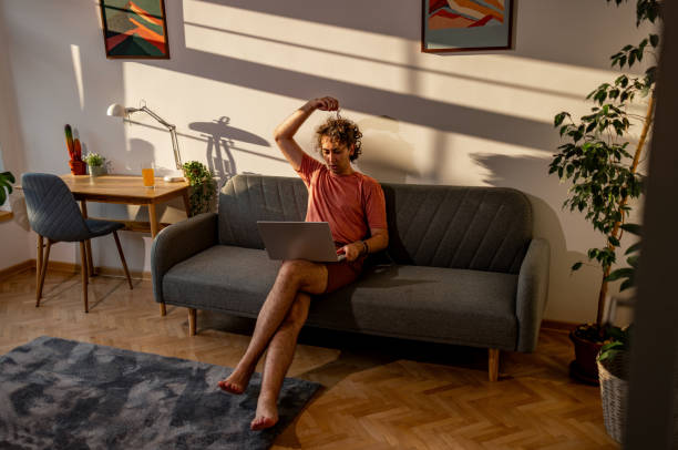 istock Student sitting on a sofa in his apartment and using lap top 2204396614