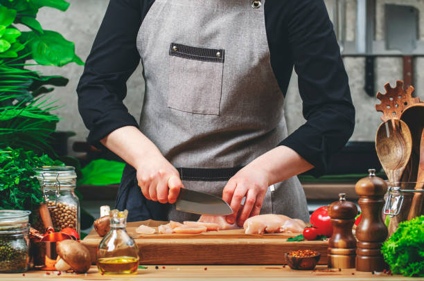 istock Chef cuts raw chicken fillet with santoku knife doing strips. Cozy kitchen with wooden table, kitchenware, vegetables, herbs and ingredients for cooking. Healthy eating, culinary, recipes, food blogging 2204402051