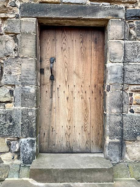 A weathered wooden door with iron handle set in an aged stone wall, showing rustic medieval craftsmanship and historical charm