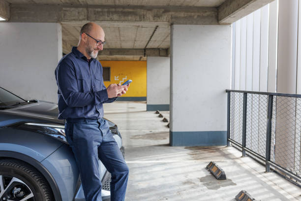 istock Mature man using phone while leaning on the car in a parking garage 2204407503