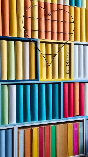 istock Library, colorful generic book spines in shelves, wire heart shape hanging at it 2204411006