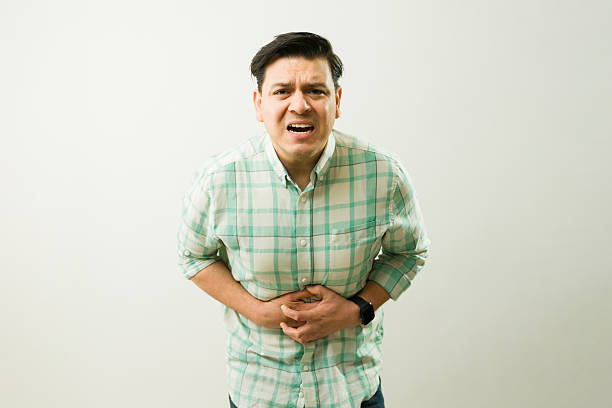istock Ill man experiencing severe abdominal pain, holding his belly with both hands and grimacing in discomfort 2204413378