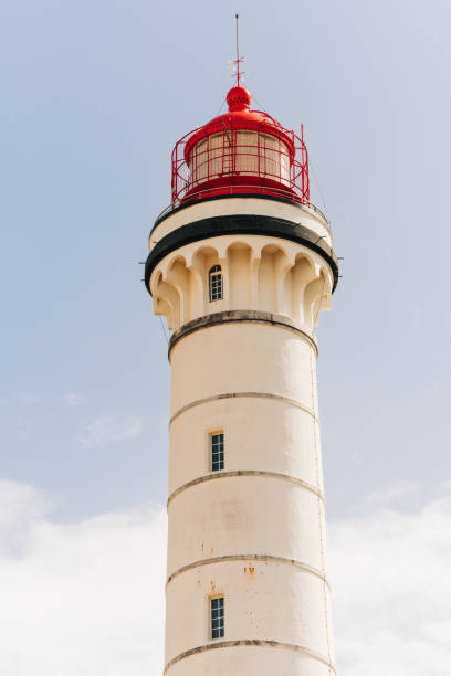 istock Tall white lighthouse with a red dome and railing stands against a clear blue sky. 2204417999