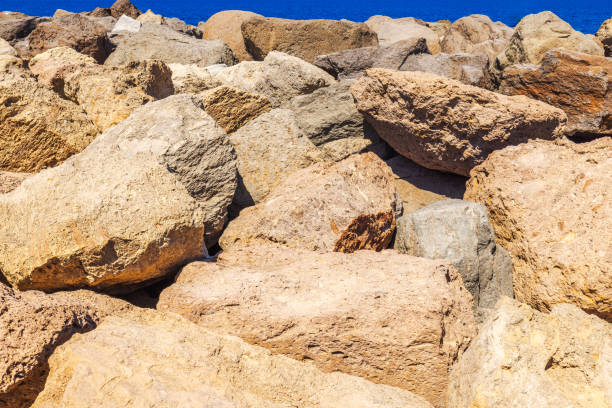 Large rugged rocks on Atlantic Ocean shore in Gran Canaria under bright sunlight with deep blue ocean in background.