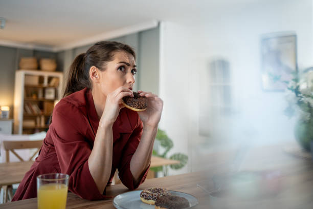 istock Young woman indulging in chocolate donuts at home 2204426510