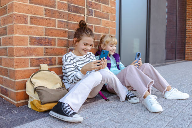 istock Two children sitting outside using smartphones and enjoying their free time 2204426894