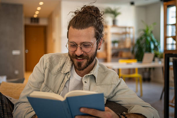 istock Young man reading a book and smiling at home 2204427368