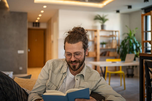 istock Young man reading a book and smiling at home 2204427373