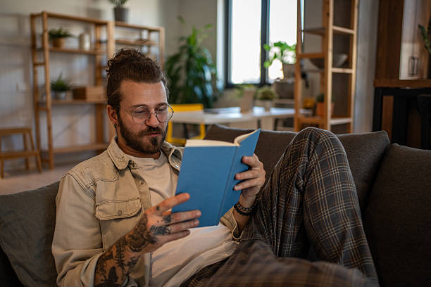 istock Young man relaxing on sofa reading a book at home 2204427406