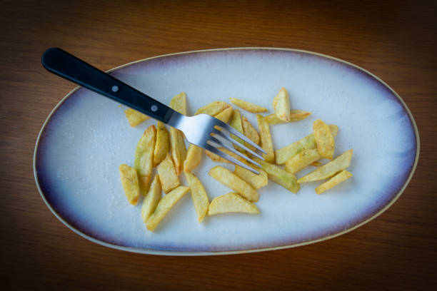 Potato wedges and fork left on dinner plate. Nobody.