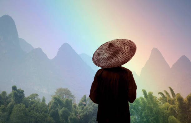 China Guilin, Chinese farmer in big straw hat lookiing out at rainbow mountains.  composite image