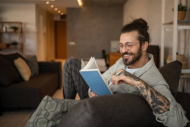 istock Young man relaxing on sofa reading a book at home 2204436950
