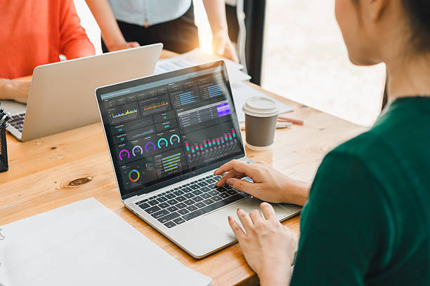 istock woman working on laptop displaying colorful data analytics and graphs, with colleagues in background and coffee cup on wooden desk, creating collaborative workspace 2204441707