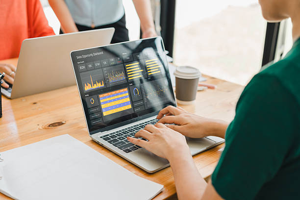 istock person working on laptop displaying data analytics and graphs on screen, with colleagues in background and coffee cup on wooden desk 2204441709