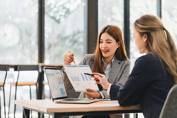istock Two businesswomen discussing financial charts and data analysis in modern office setting, with laptops and documents on table, fostering collaboration and teamwork 2204441839