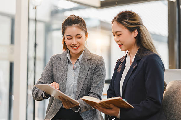 istock Two professional women in formal attire discussing work while reviewing documents in modern office setting, showcasing teamwork and collaboration 2204441968
