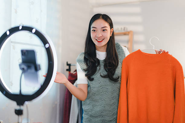 istock woman enthusiastically presenting orange sweater during live stream in bright room 2204447219