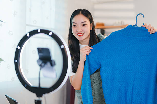 istock woman smiling while live streaming and showcasing blue sweater in bright room 2204447242