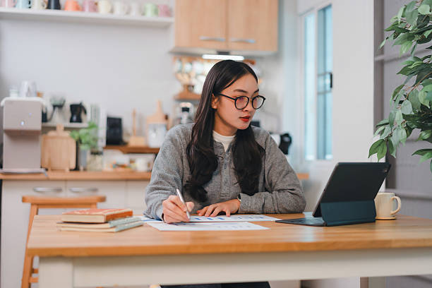 istock woman working at wooden table in cozy kitchen, using tablet and writing notes 2204447534