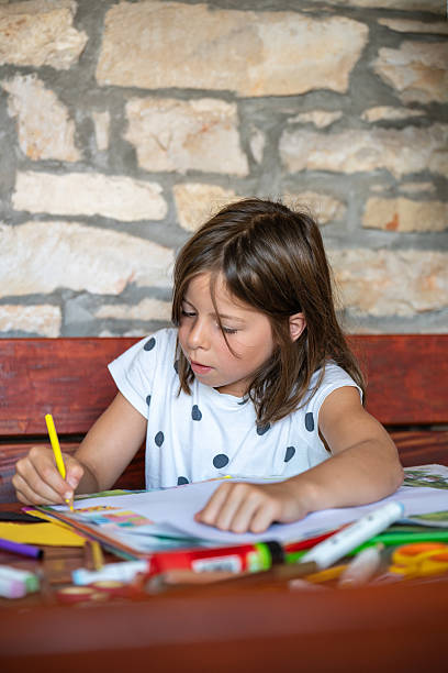 istock Enthusiastic girl draws picture while sitting at table in comfort her home. Bright colored pencils lie nearby. On childs face - concentration. Childhood, creativity, development imagination. 2204448115