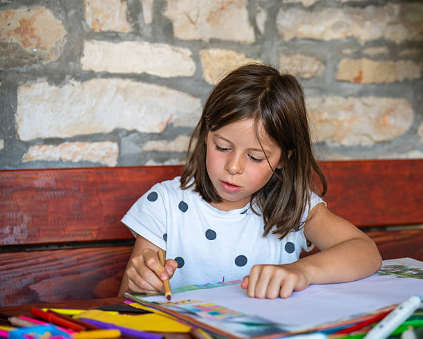 istock Enthusiastic girl draws picture while sitting at table in comfort her home. Bright colored pencils lie nearby. On childs face - concentration. Childhood, creativity, development imagination. 2204448120