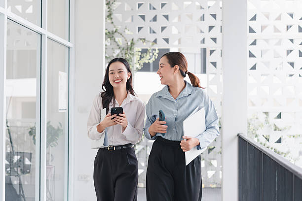 istock Two professional women walking in modern office hallway, smiling and engaged in conversation 2204449155