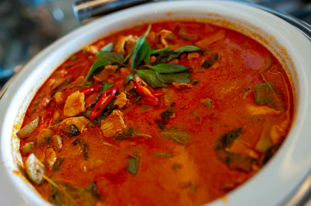 A close-up of a vibrant spicy soup in a bowl, featuring fresh herbs, tender meat, and chili peppers, perfect for a comforting meal.